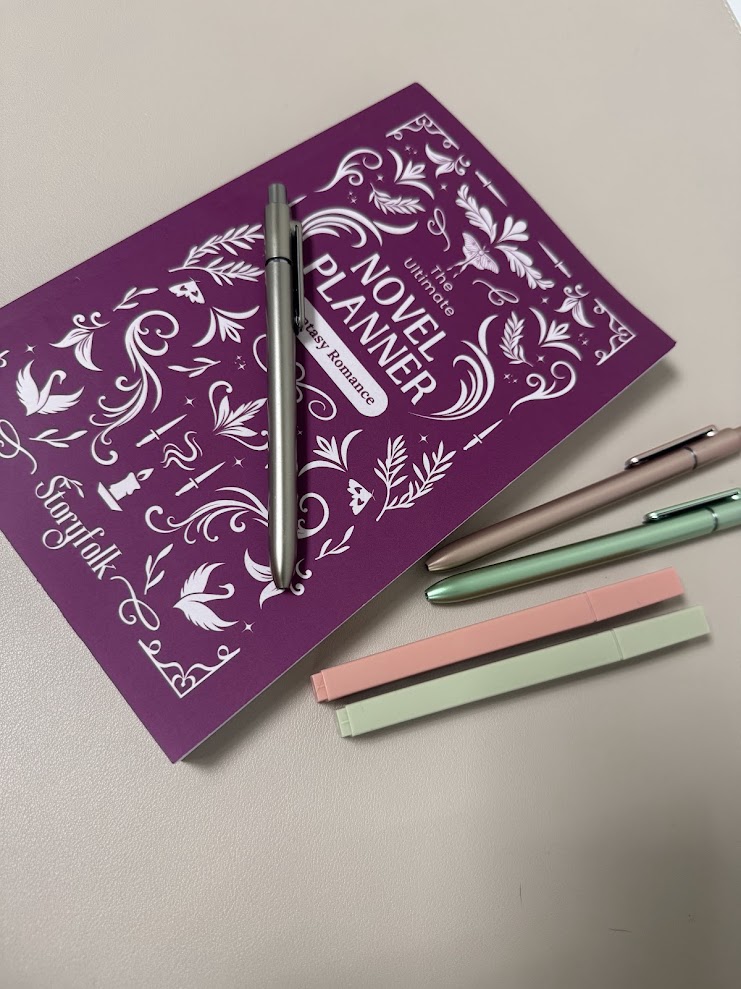 A fantasy romance novel planner with pens and muted highlighters on a cream desk